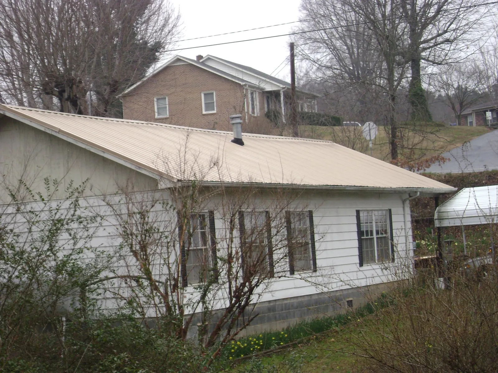 Tan metal roof on a white sided house set into a hillside — Commercial Roofing by Roofing Brothers in Plymouth